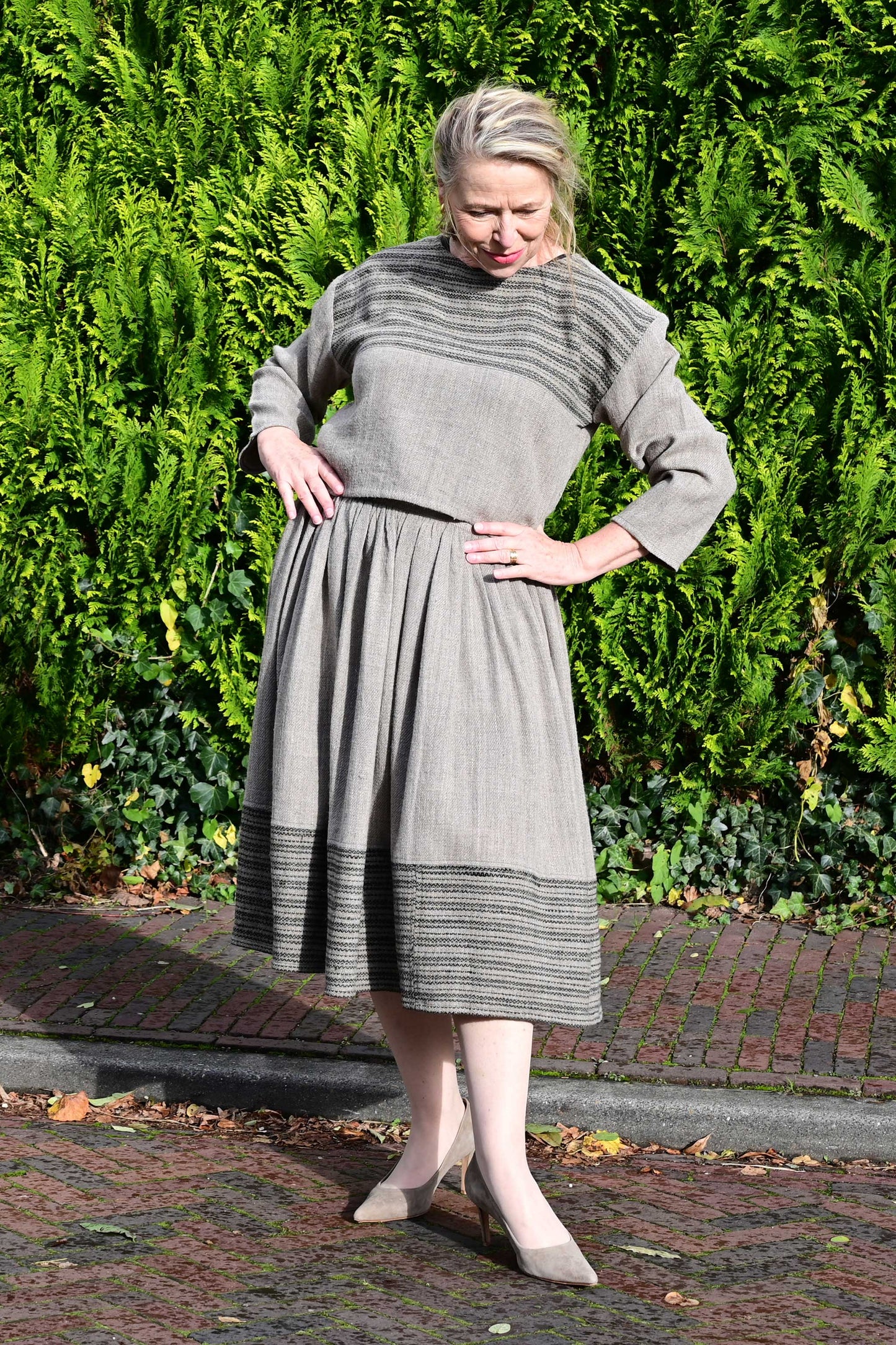 Front pose of a middle aged female model wearing a handspun handwoven khadi full sleeved crop top for ladies in natural brown wool with black details.