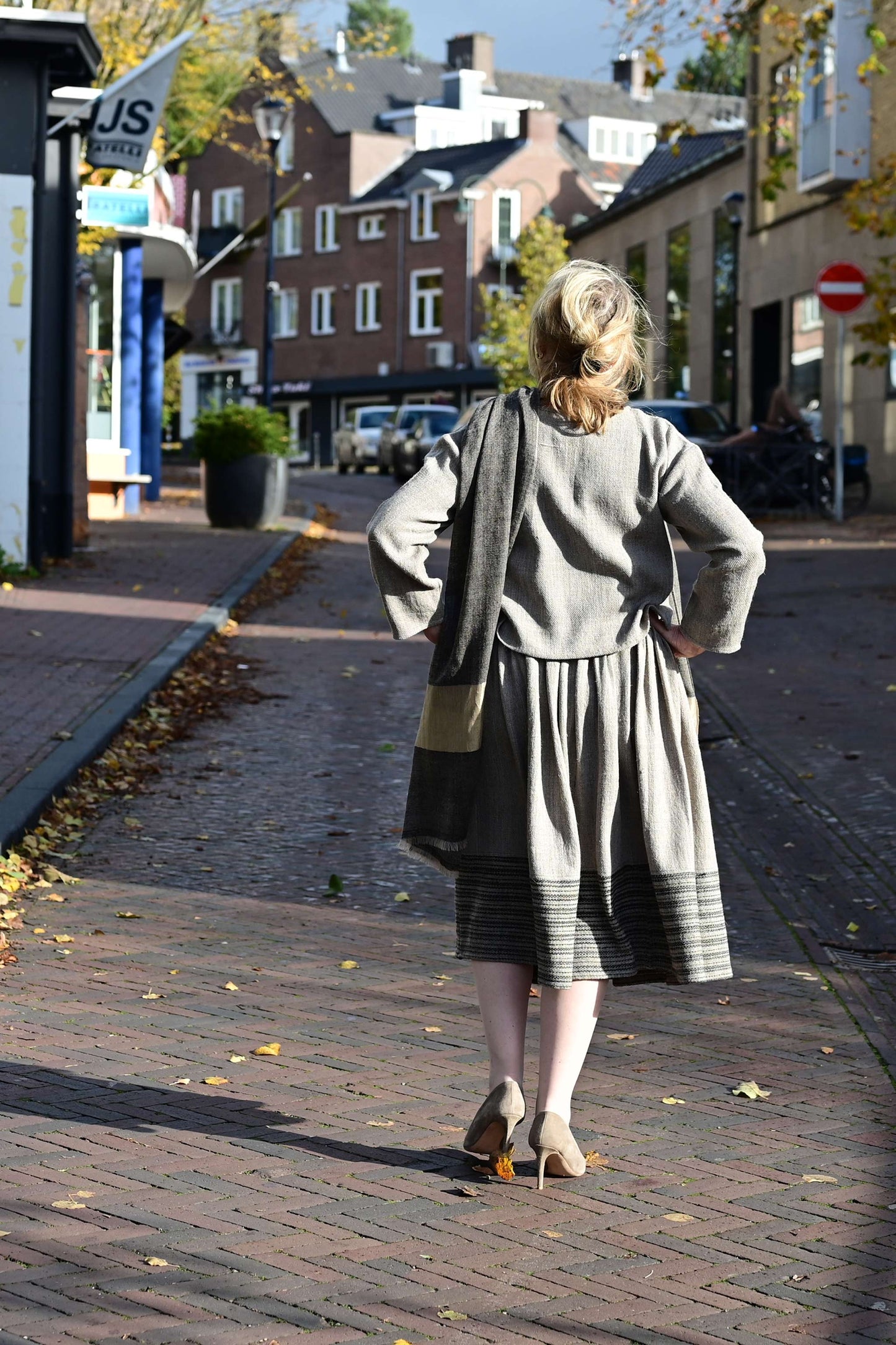 A middle aged female model walking with her back towards the camera on a european street wearing a woolen crop top and gathered skirt set handspun and hand woven by Cotton Rack.