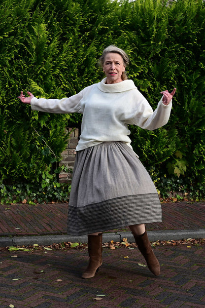 Creative Pose of a dancing middle aged female model on a european street wearing an ivory white cowl neck sweater and a long gathered dress handmade by Cotton Rack.